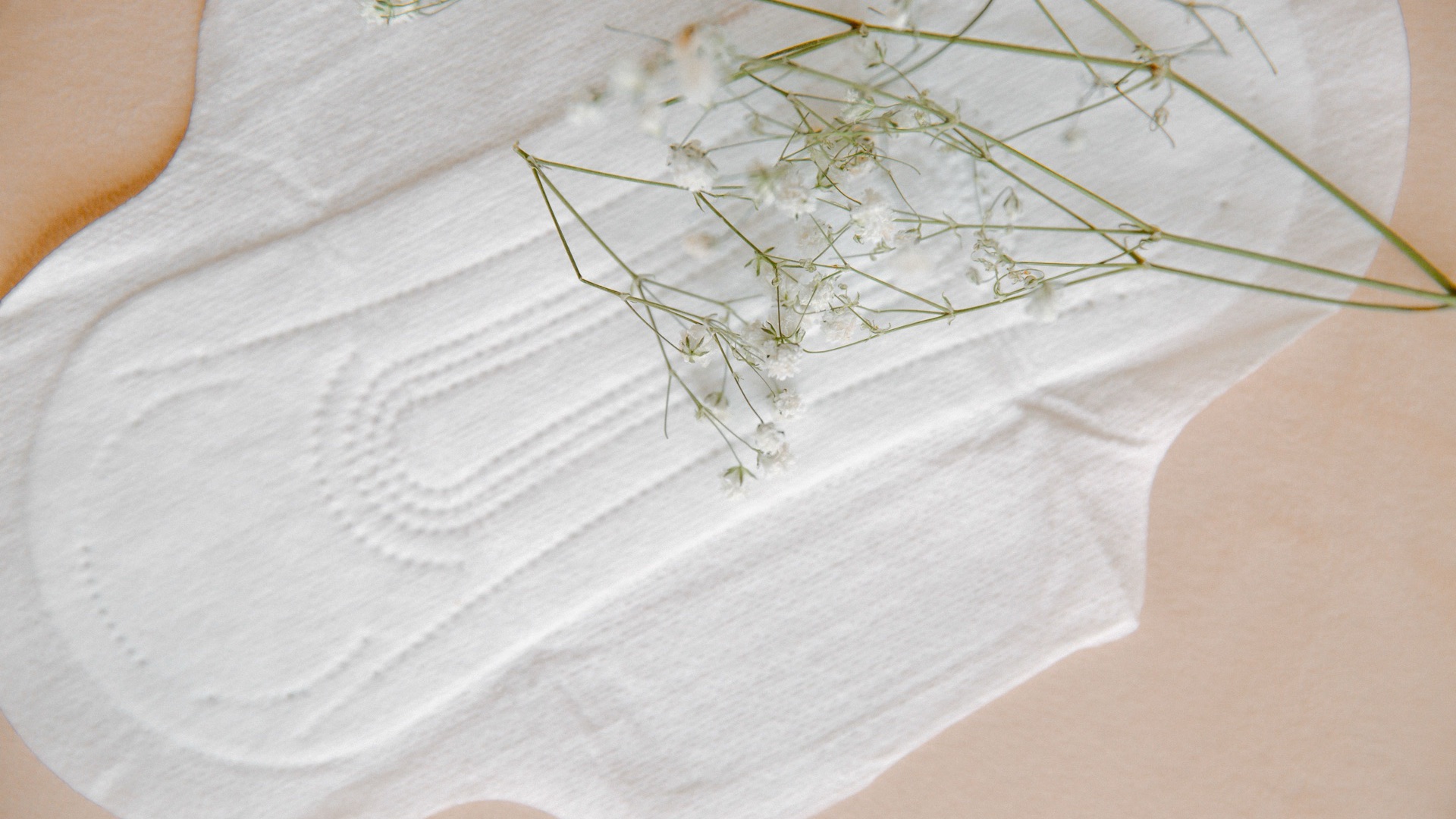 Close-up of the embossed topsheet of a white sanitary pad, with sprigs of gypsophila