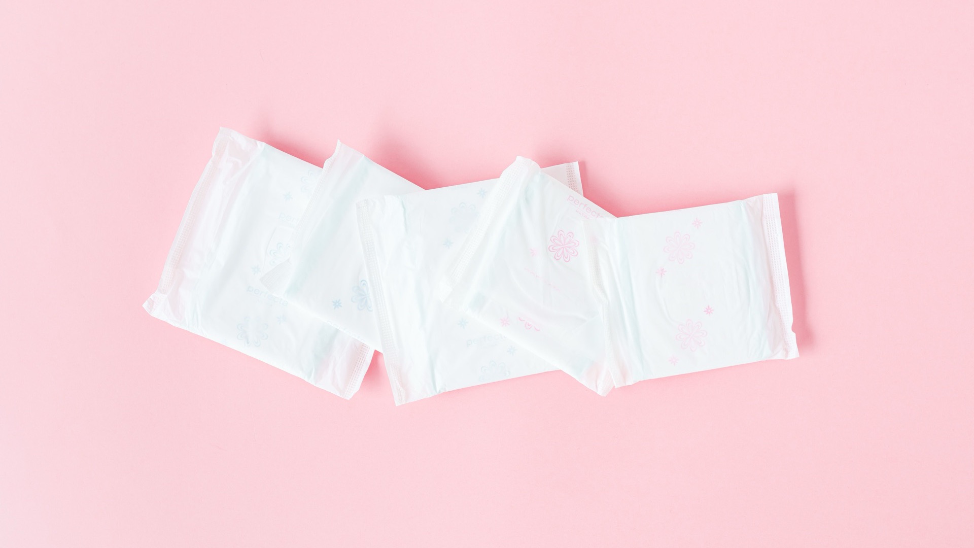 Four individually wrapped panty liners on a pink background