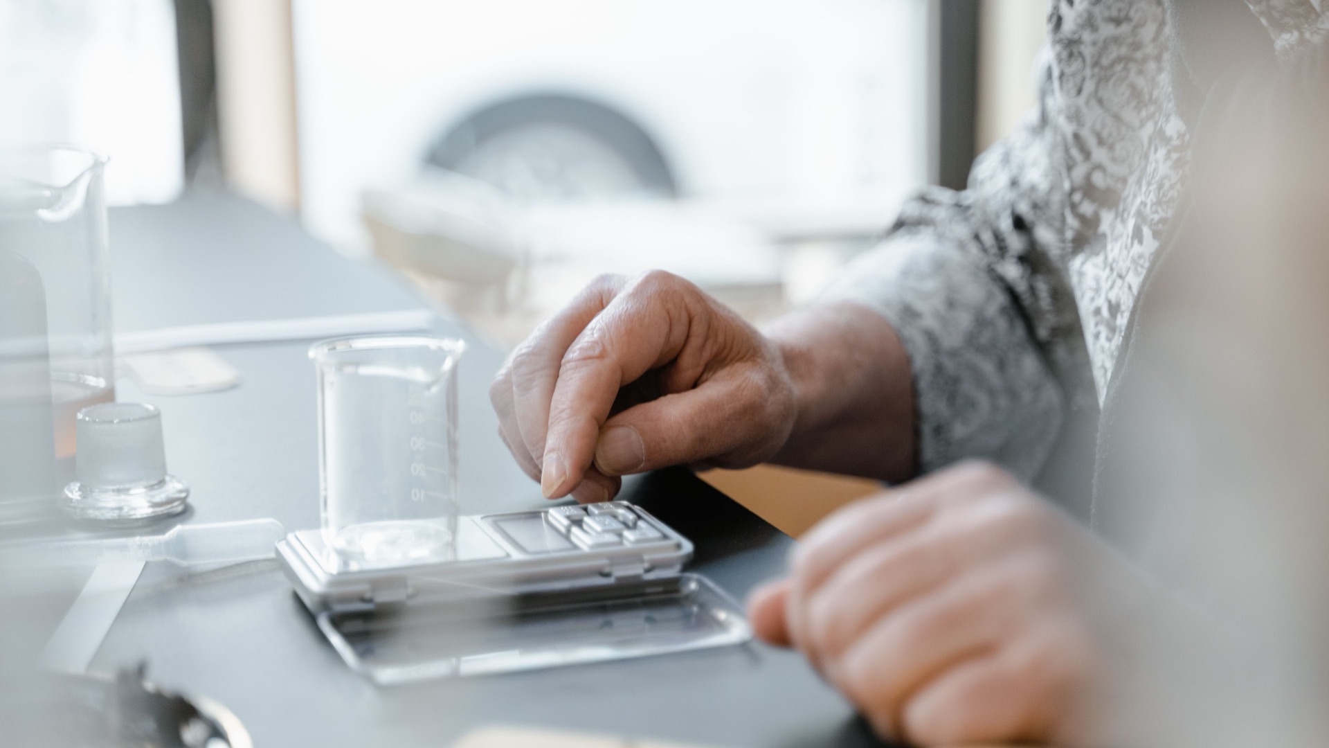 A hand adjusting a digital scale next to a glass beaker